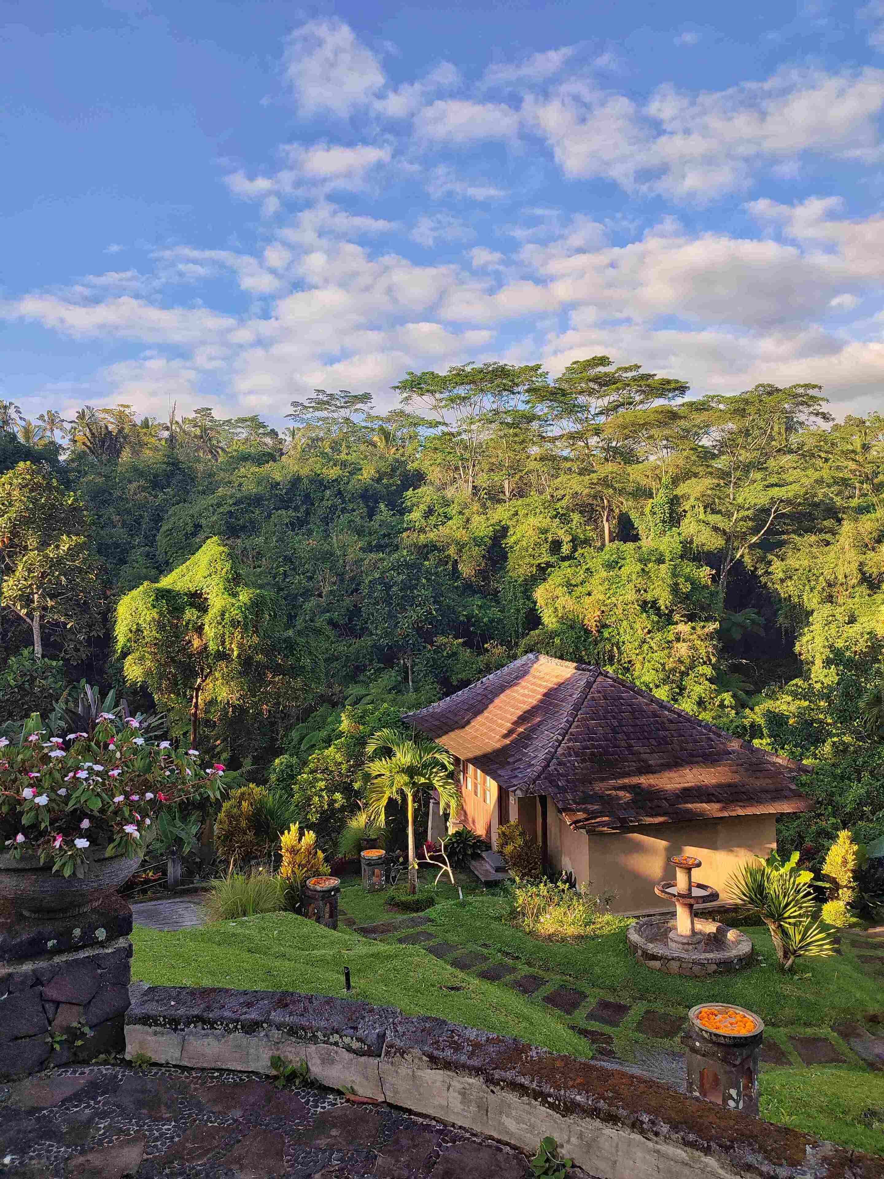 A traditional house with a tiled roof surrounded by lush greenery and a stone wall.