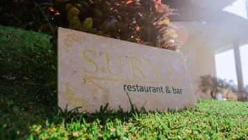 A sign for 'Surya restaurant & bar' on a grassy area with plants in the background.