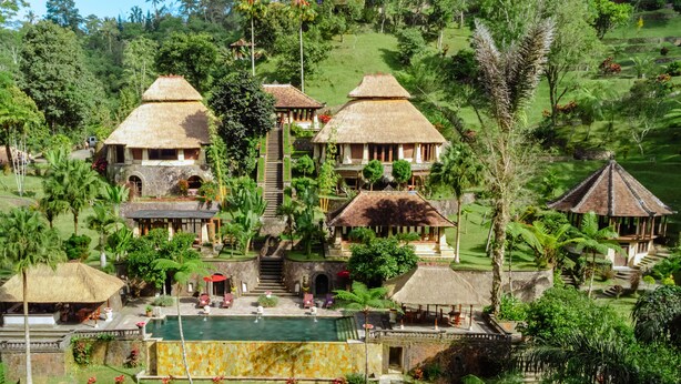 Ein Resort mit mehreren Gebäuden mit Strohdächern, einem zentral gelegenen Pool und üppiger Bepflanzung.