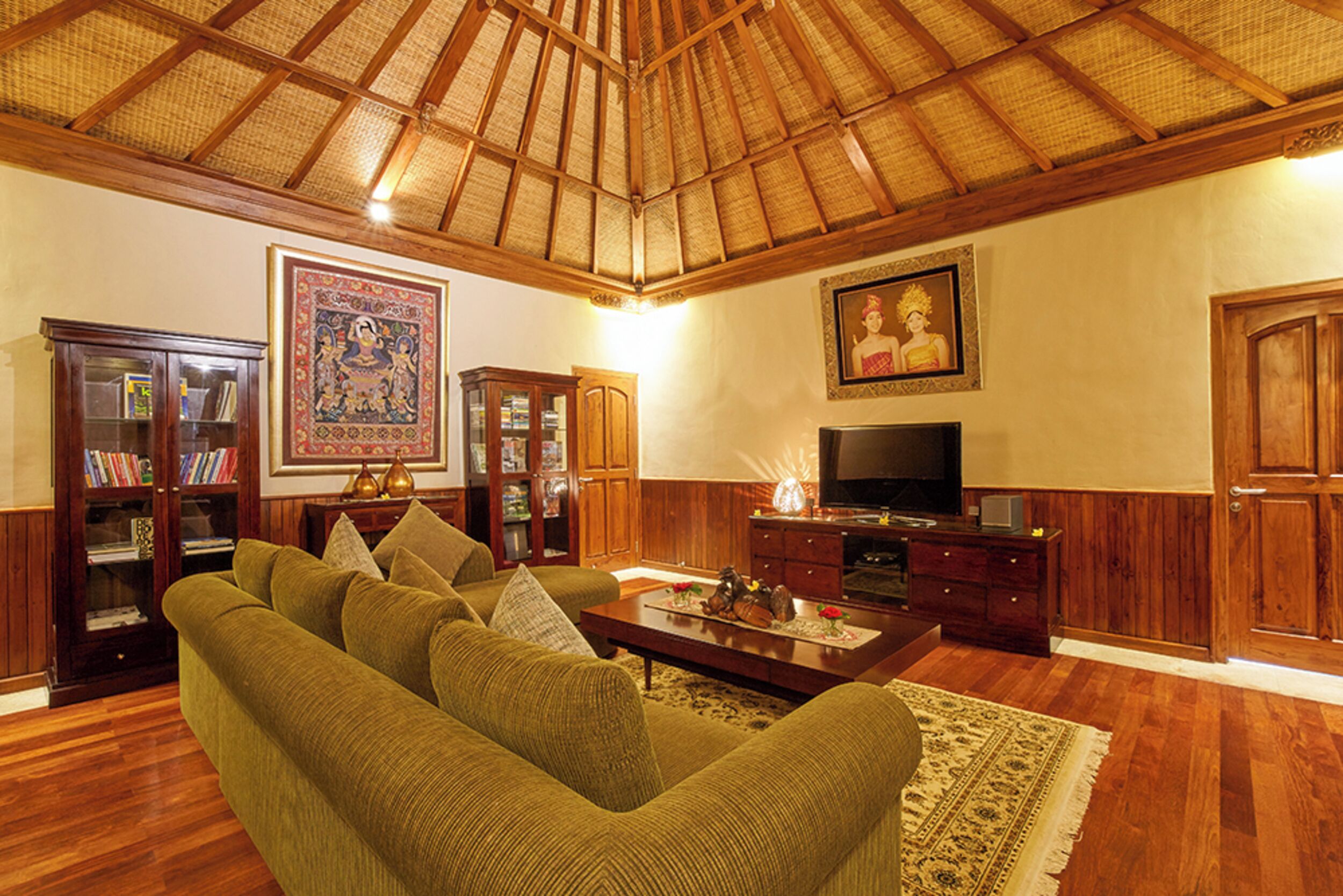 A living room with a high wooden ceiling, a green sofa, a coffee table, a television, and wooden cabinets.