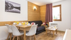 Una habitación acogedora con un muro de madera, una mesa de comedor con sillas, un sofá y una ventana con cortinas.