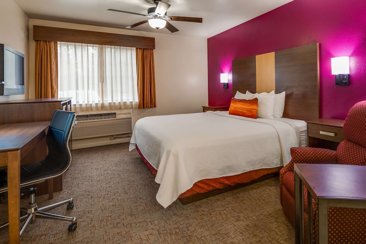 A hotel room with a bed, desk, chair, and a window with curtains.