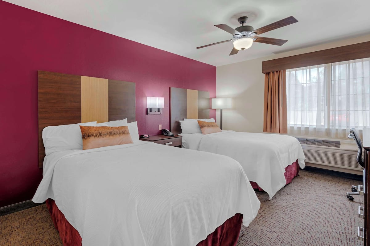 A hotel room with two beds, a ceiling fan, a nightstand with a phone, and a window with curtains.