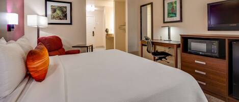 Una habitación de hotel con una cama grande, un escritorio con silla, televisor y microondas.