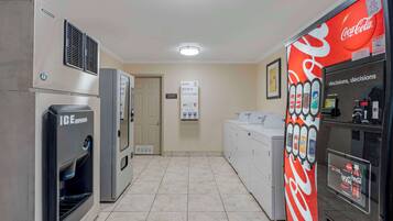 Una cocina de hotel con dispensador de hielo, un refrigerador con publicidad de Coca-Cola y un cartel para jabón, lejía y suavizantes.