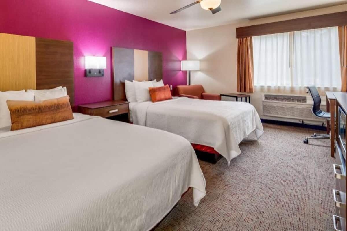 A hotel room with two beds, a desk, a chair, and a large window with curtains.