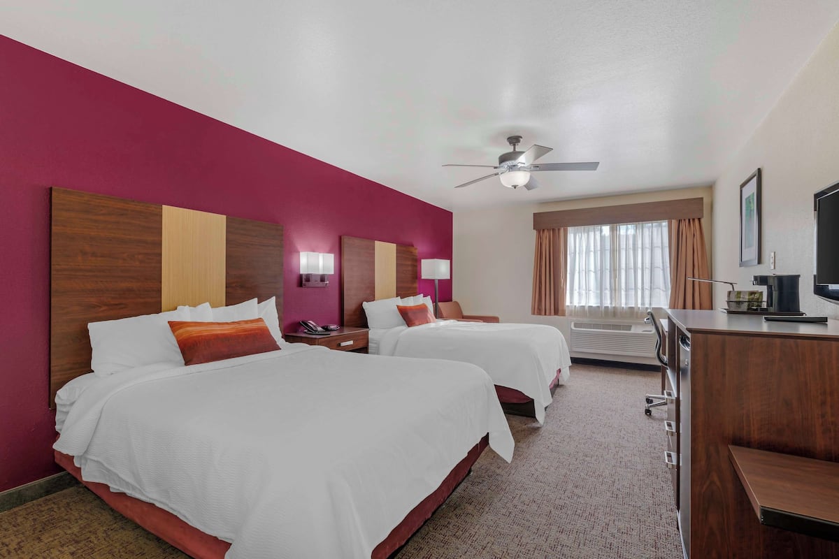 A hotel room with two beds, a desk, a ceiling fan, and a window with curtains.
