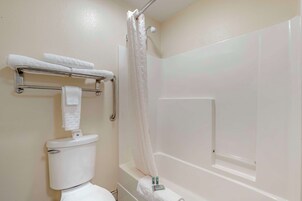 Un baño con inodoro, toallero con toallas, cortina de ducha y bañera.
