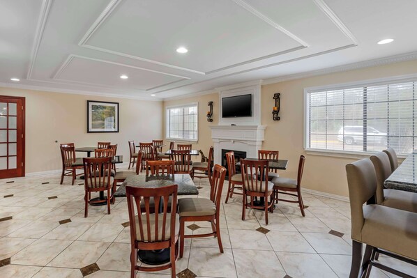 A spacious dining area with multiple wooden tables and chairs, a fireplace, and a flat-screen TV mounted above it. - Best Western Pineywoods Inn (Atlanta)