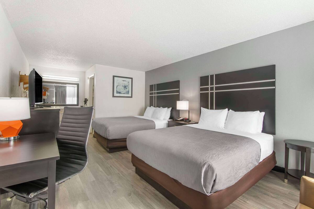 A hotel room with two beds, a desk with a chair, a TV, and a window with curtains.