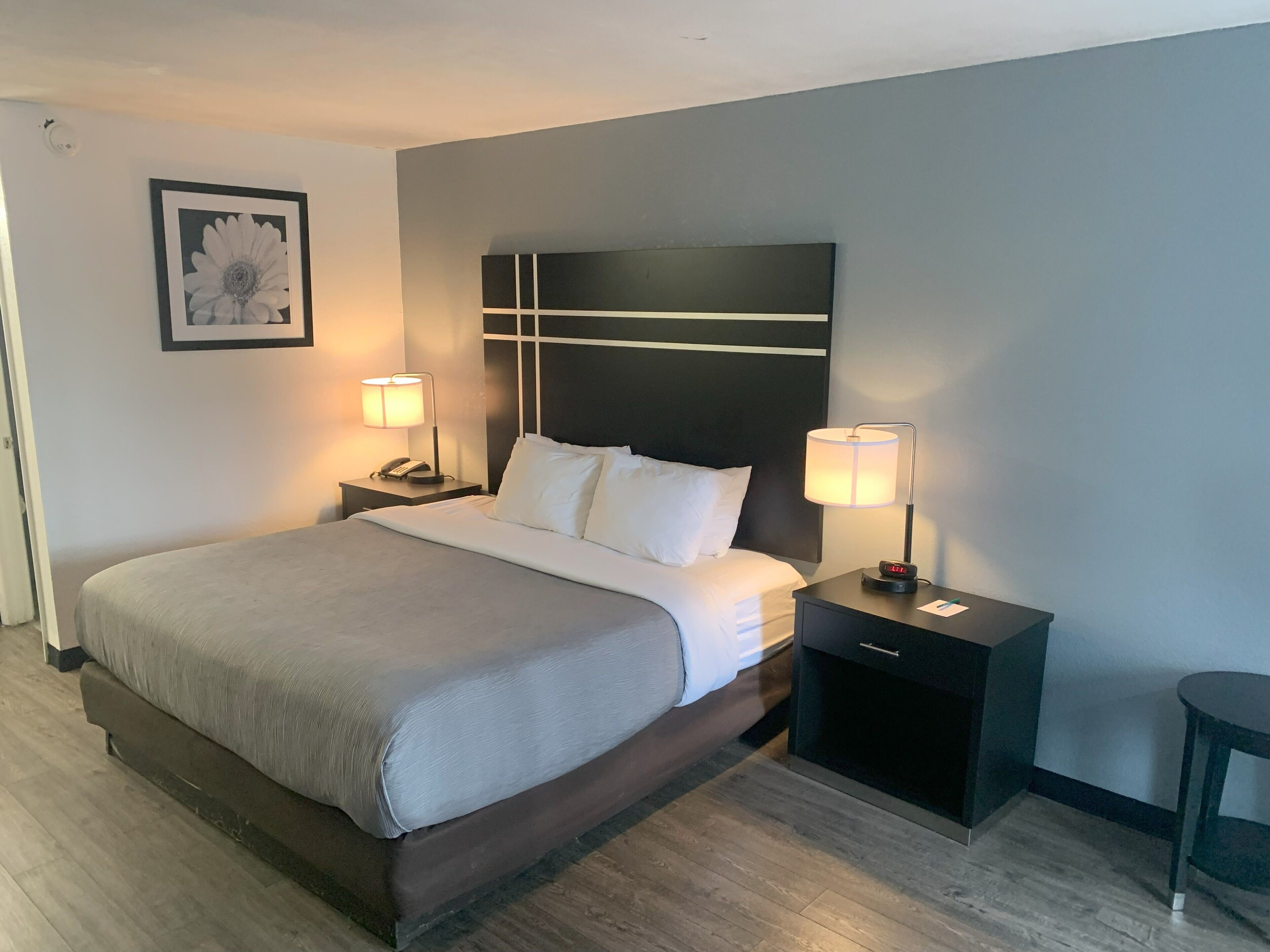 A hotel room with a large bed, two bedside tables with lamps, a nightstand with a phone, and a framed picture on the wall.
