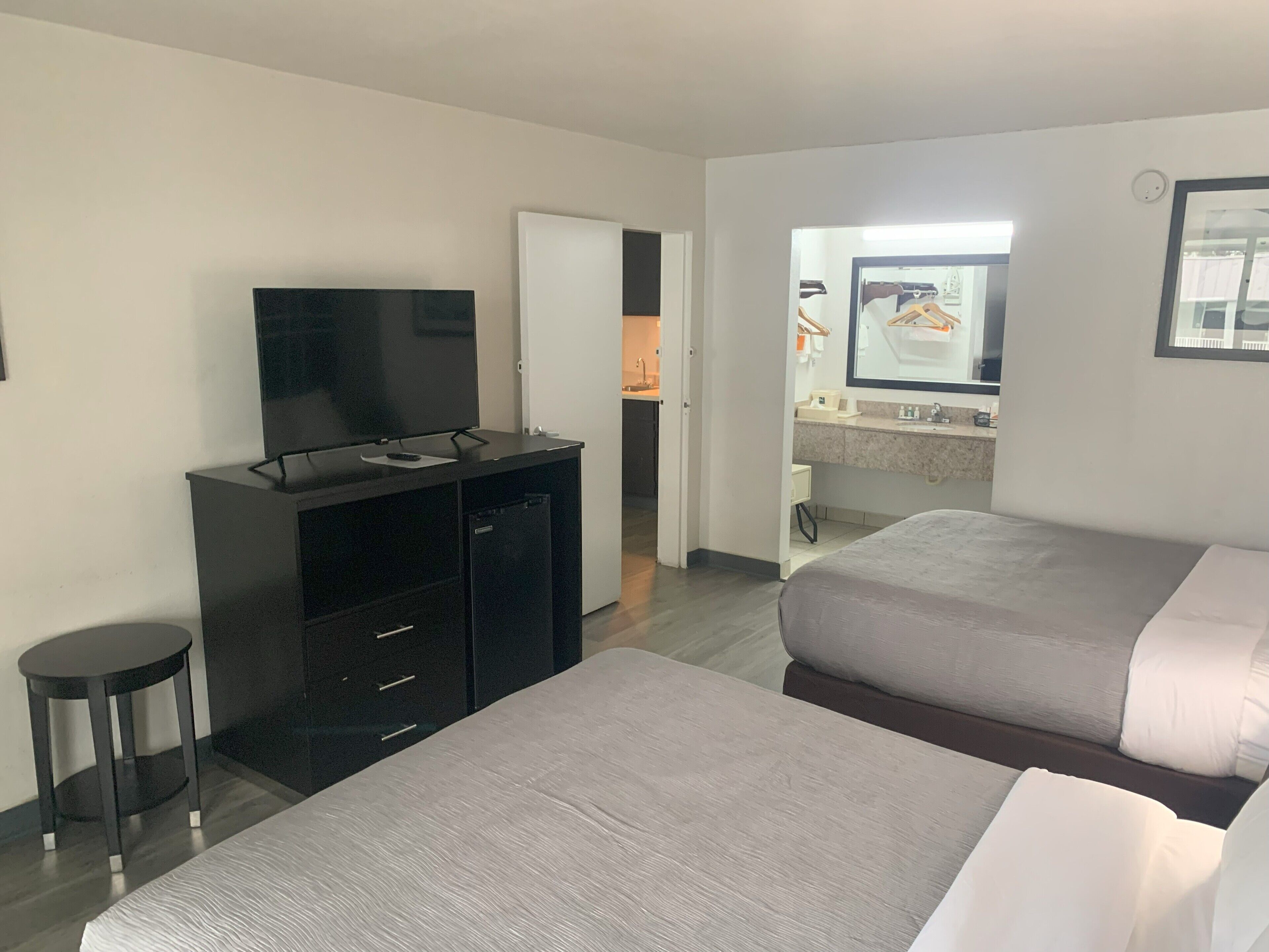 Une chambre d’hôtel avec deux lits, un téléviseur posé sur un meuble, un petit tabouret et une salle de bain visible à travers une porte ouverte.