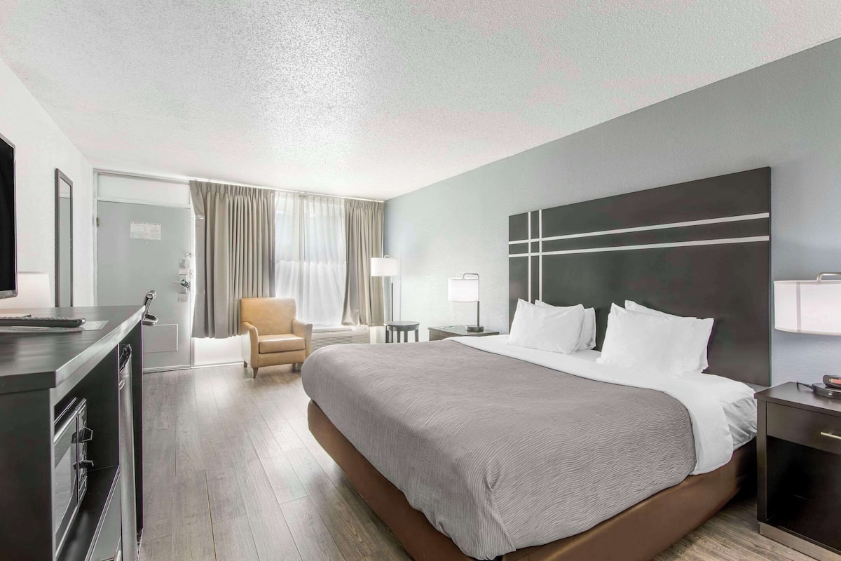 A modern hotel room with a large bed, a desk, a chair, and a television.
