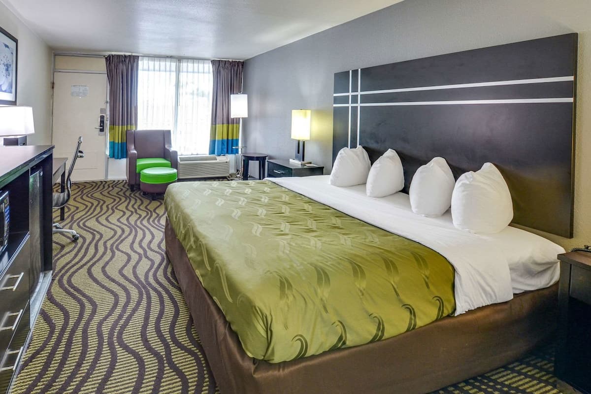 A hotel room with a bed, a desk, a chair, a TV, and a window with curtains.