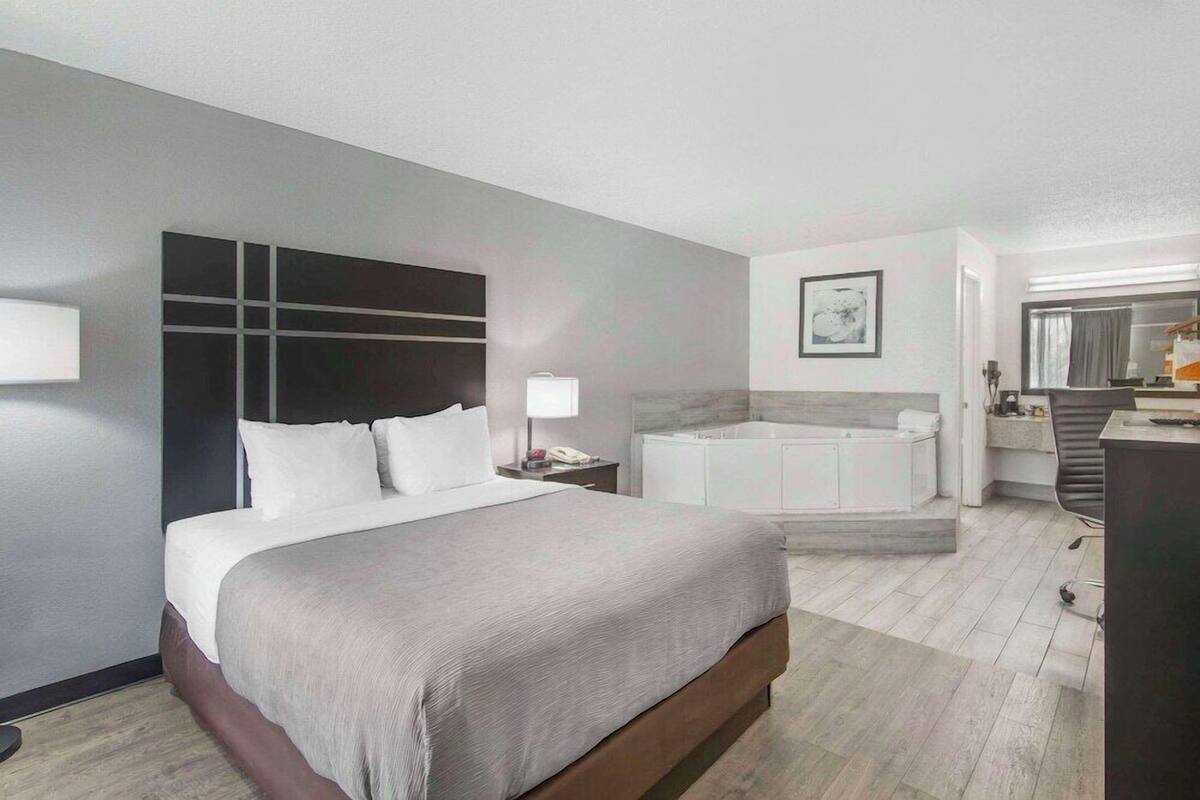 A modern hotel room with a large bed, a separate bathroom with a bathtub, and a desk with a chair.