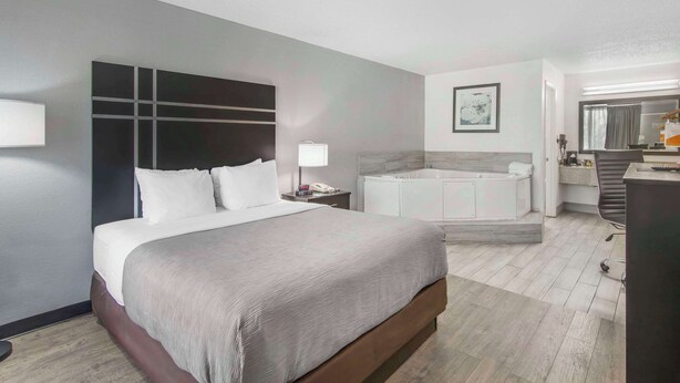 Quarto de hotel moderno com uma cama grande, banheiro separado com banheira e uma mesa de trabalho com cadeira.
