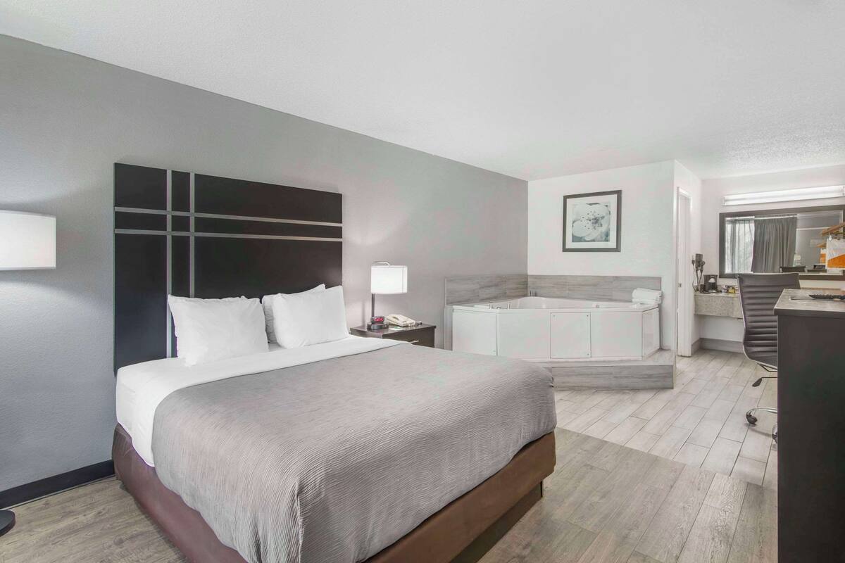 A modern hotel room with a large bed, a separate bathroom with a bathtub, and a desk with a chair.