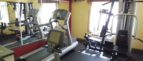 A gym with treadmills, a weight machine, and a television on the wall.