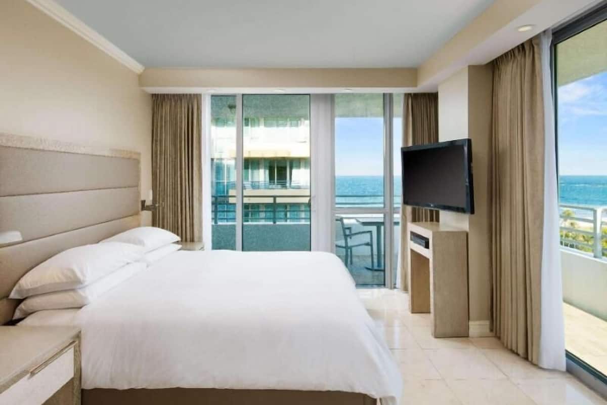 Habitación de hotel con una cama grande, televisión y balcón con vista al océano.