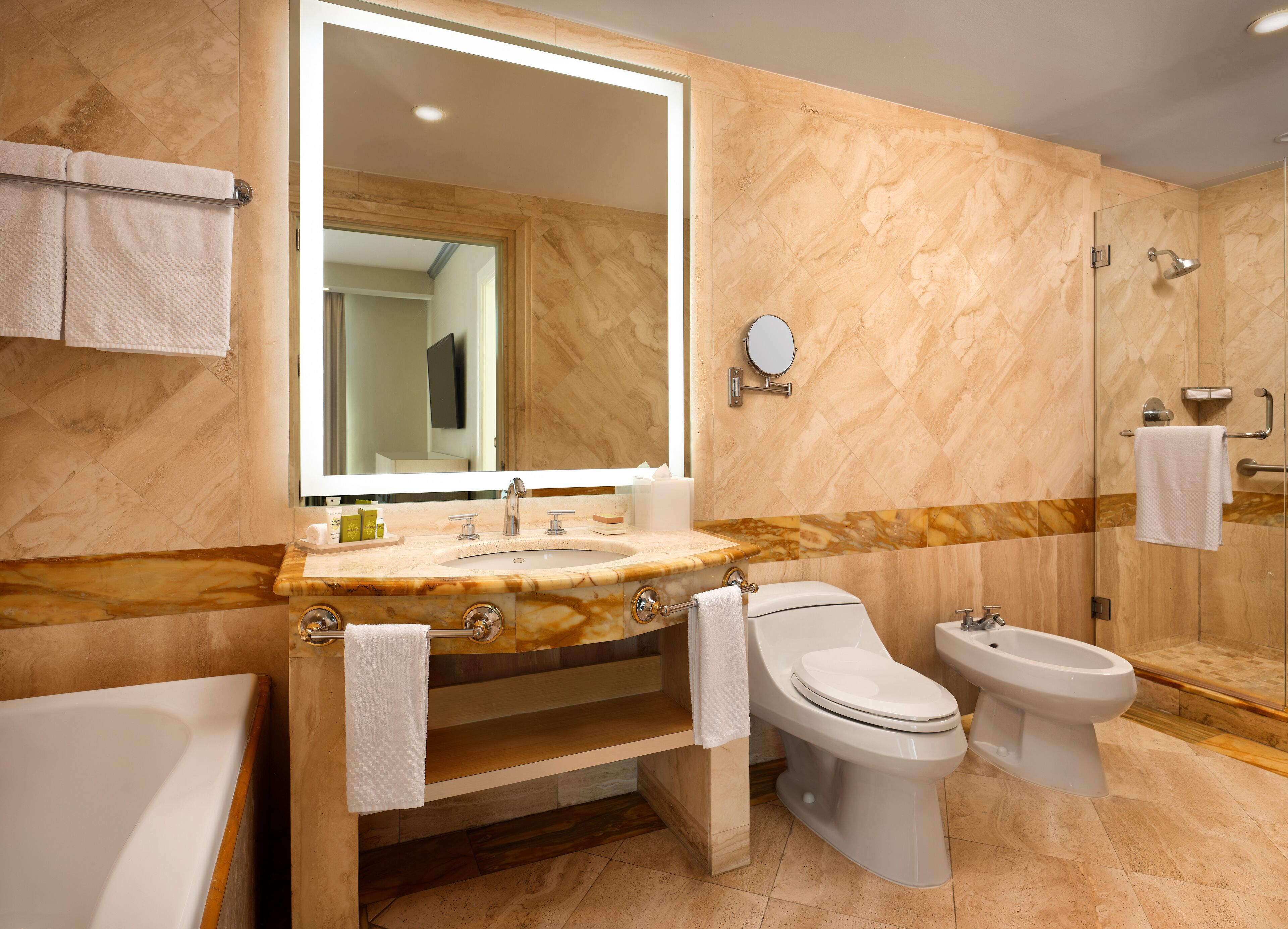 A bathroom with a marble vanity, a large mirror, a toilet, a bidet, and a bathtub.