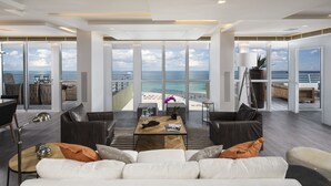 A spacious living area with a large window overlooking a beach, furnished with a sofa, coffee table, and chairs. - Hilton Bentley Miami/South Beach (Miami Beach)