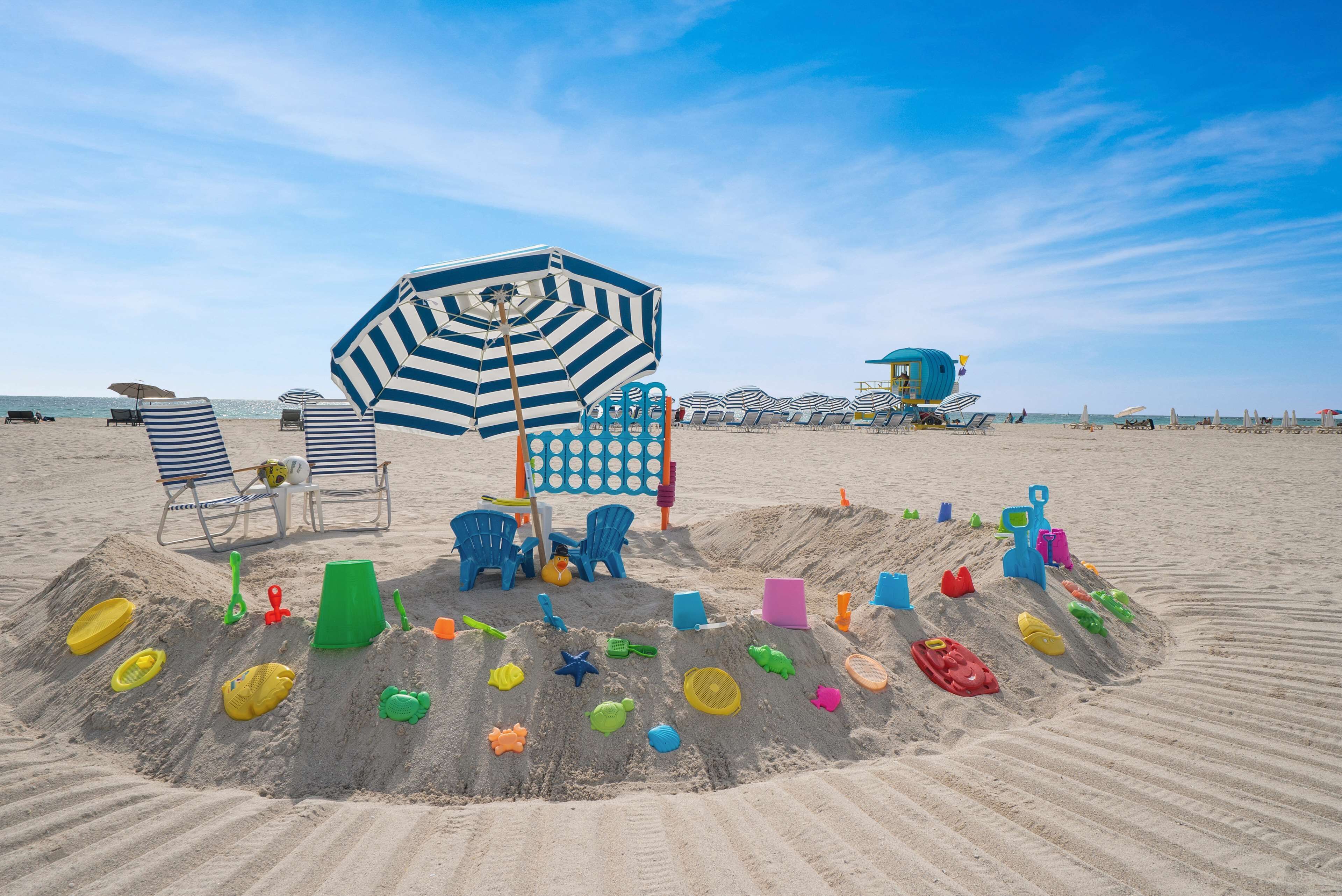 Una playa arenosa con sombrillas de playa a rayas, sillas de descanso y una torre de salvavidas.