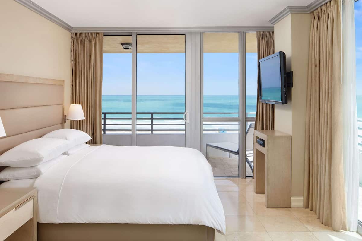 A hotel room with a large bed, a TV, and a view of the ocean.