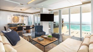 A modern living room with a large window overlooking the beach, a flat-screen TV mounted on the wall, and a cozy seating area with a coffee table. - Hilton Bentley Miami/South Beach (Miami Beach)