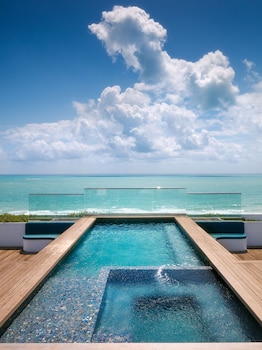 A spacious living area with a large window overlooking a beach, furnished with a sofa, coffee table, and chairs. at Hilton Bentley Miami/South Beach