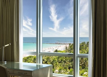 A modern living room with a large window overlooking the beach, a flat-screen TV mounted on the wall, and a cozy seating area with a coffee table. at Hilton Bentley Miami/South Beach