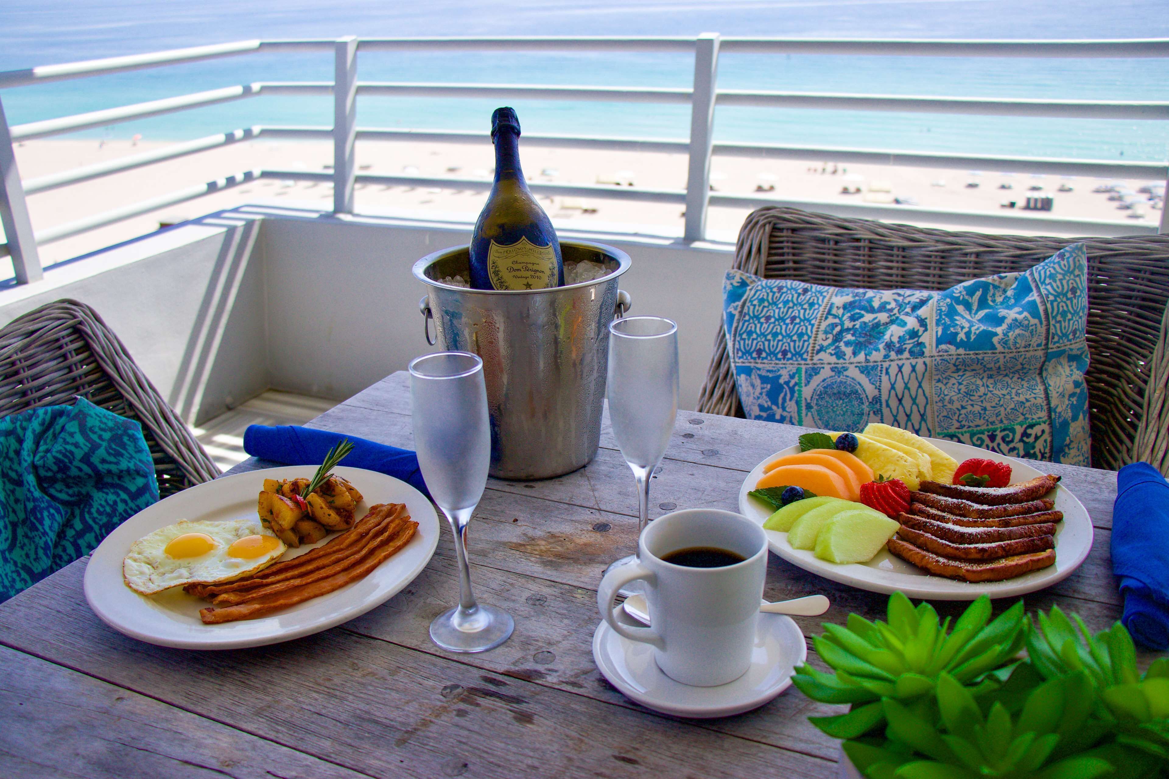 Ein Tisch mit Frühstücksleckereien, einer Champagnerflasche und Blick auf den Strand.