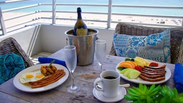 Ein Tisch mit Frühstücksleckereien, einer Champagnerflasche und Blick auf den Strand.