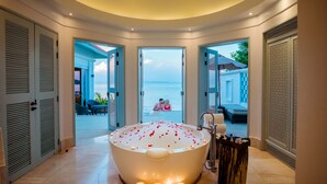 Una bañera grande con velas y pétalos de rosa, rodeada de puertas que dan a una zona de piscina.