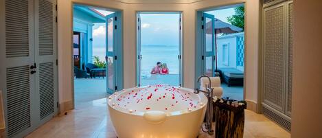 A large bathtub with candles and rose petals, surrounded by doors leading to a pool area.