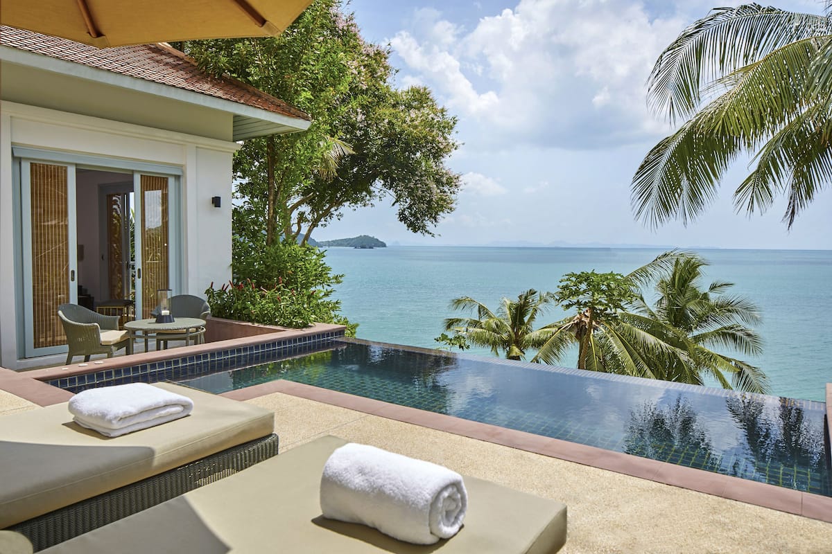 A poolside area with lounge chairs, a small table, and a view of the sea.