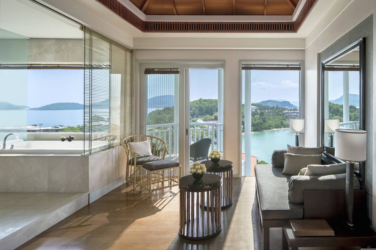 A spacious balcony with a view of the sea and mountains, furnished with a sofa, chairs, and a small table.