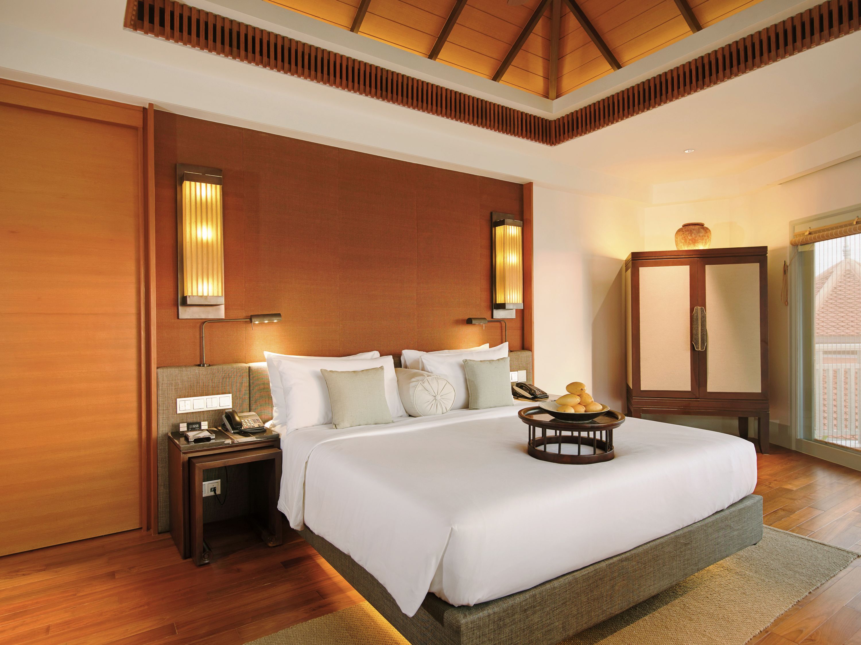 A spacious bedroom with a large bed, wooden headboard, bedside lamps, and a nightstand with a telephone.