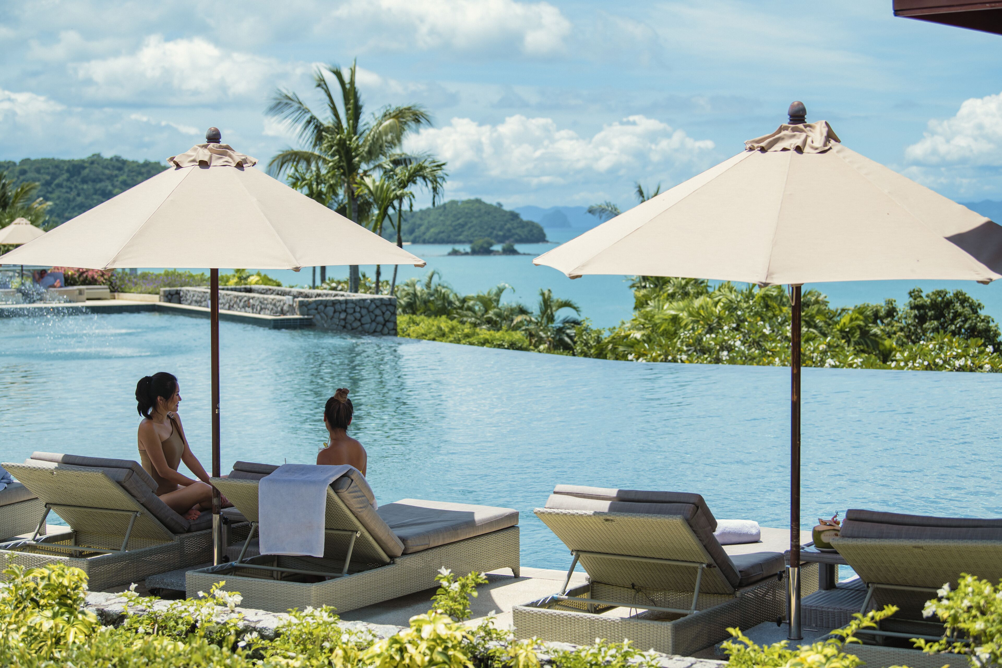 A poolside area with lounge chairs and umbrellas, overlooking a body of water and greenery.