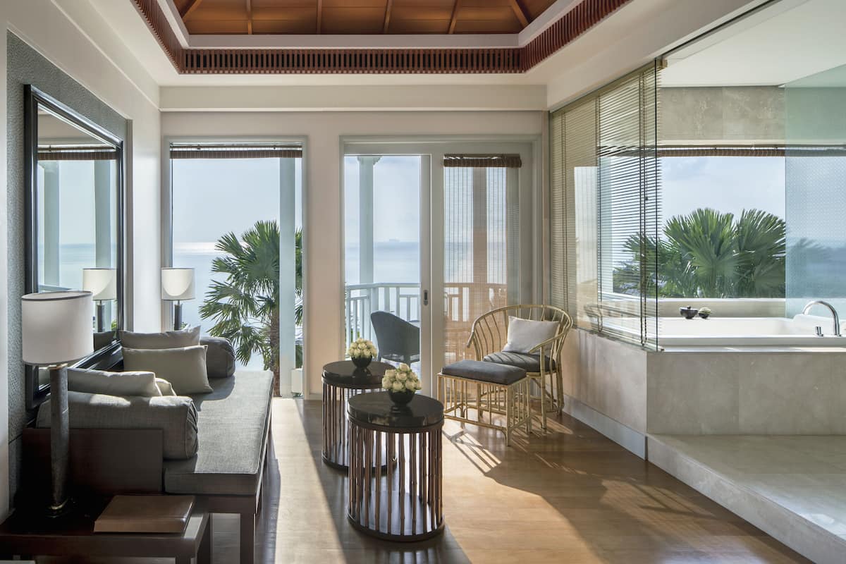 A modern hotel room with a balcony, a sofa, a dining table, and a view of the sea.