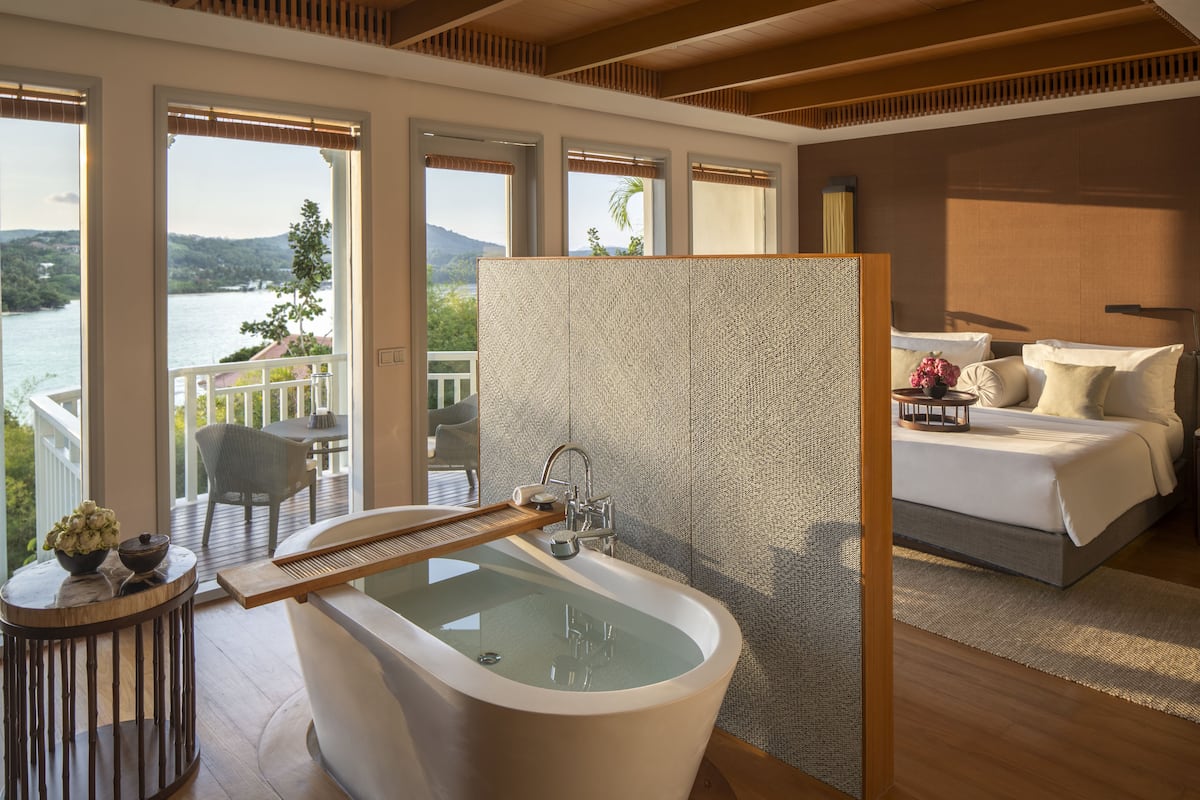 A modern bedroom with a large bed, a bathtub, and a balcony with a view of the water.