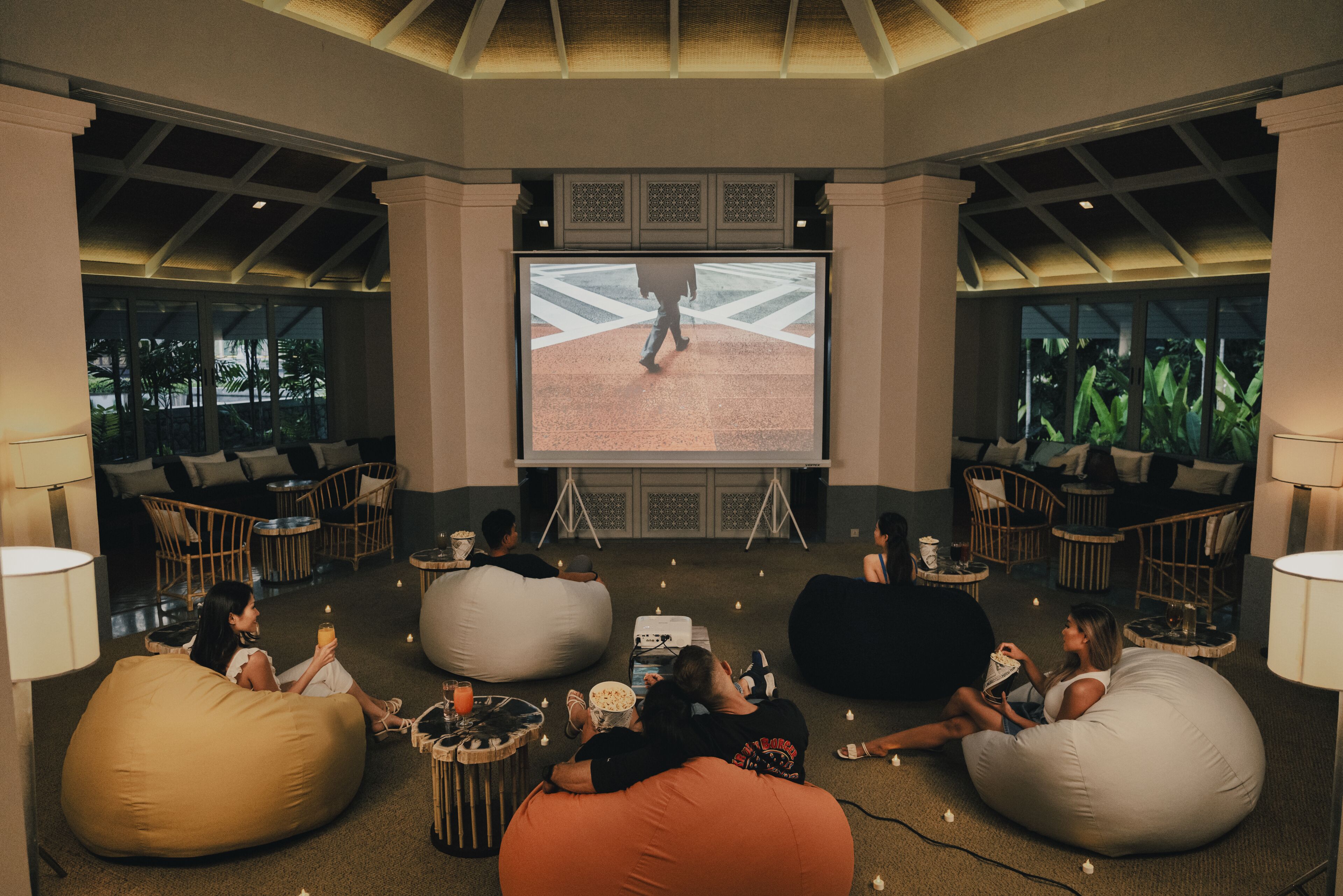 A spacious lounge area with bean bags and seating, a large screen for viewing, and a tropical view through the windows.