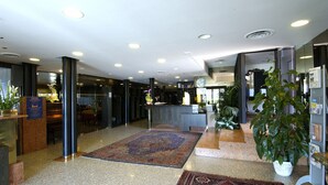 Eine Hotelhalle mit einer Rezeption, einem großen Teppich und mehreren Blumentöpfen.