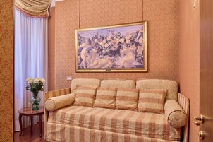 Una habitación con sofá, un cuadro enmarcado, un jarrón con flores y un papel tapiz decorado.