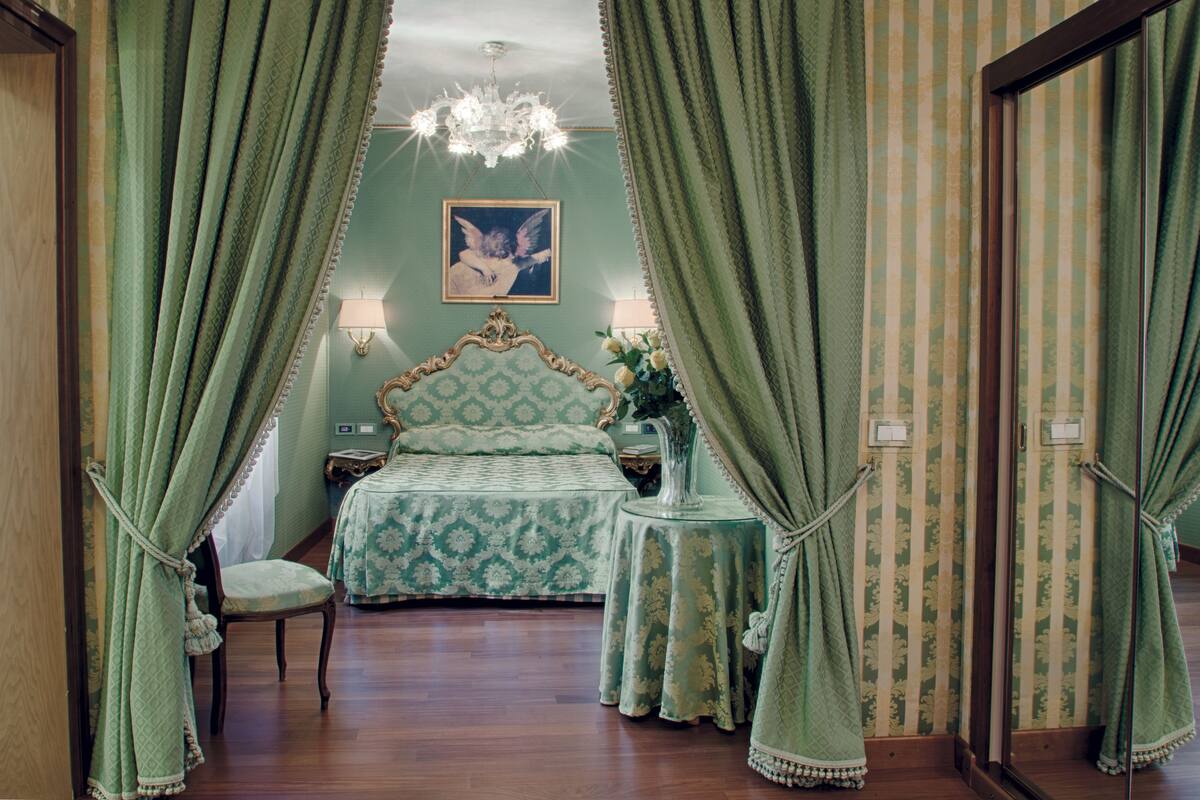 Un dormitorio con cama, una silla, una mesita de noche, una lámpara y un candelabro.