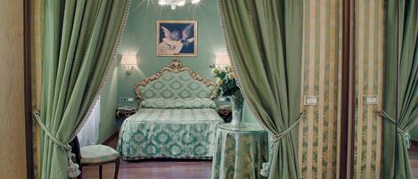 A bedroom with a bed, a chair, a nightstand, a lamp, and a chandelier.
