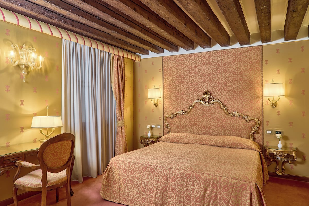 Une chambre d’hôtel comprenant un lit, un bureau, une chaise et deux tables de chevet avec des lampes.