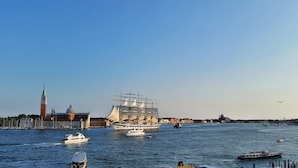 Un barco histórico de gran tamaño atracado en un puerto con un paisaje urbano al fondo.