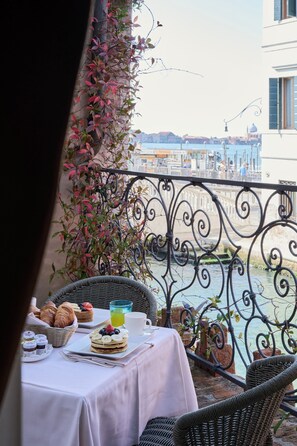Un balcón con una mesa dispuesta para el desayuno, con vistas a un canal y edificios al fondo.
