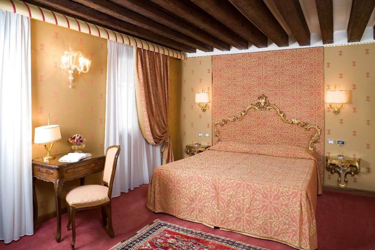 Una habitación de hotel con una cama grande, un escritorio con lámpara, una silla y una lámpara de pared decorativa.