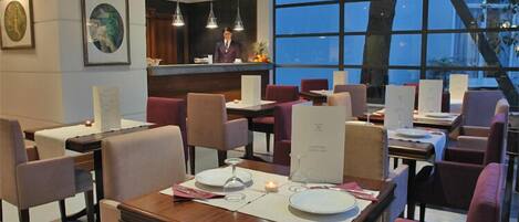A restaurant with tables set for dining, a bar area, and a view through large windows.